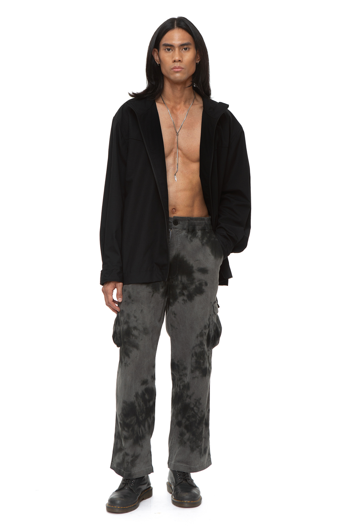 Model wearing black oversized technical jacket with high funnel neck, front zip closure, and curved seam paneling, with pocket detail.
