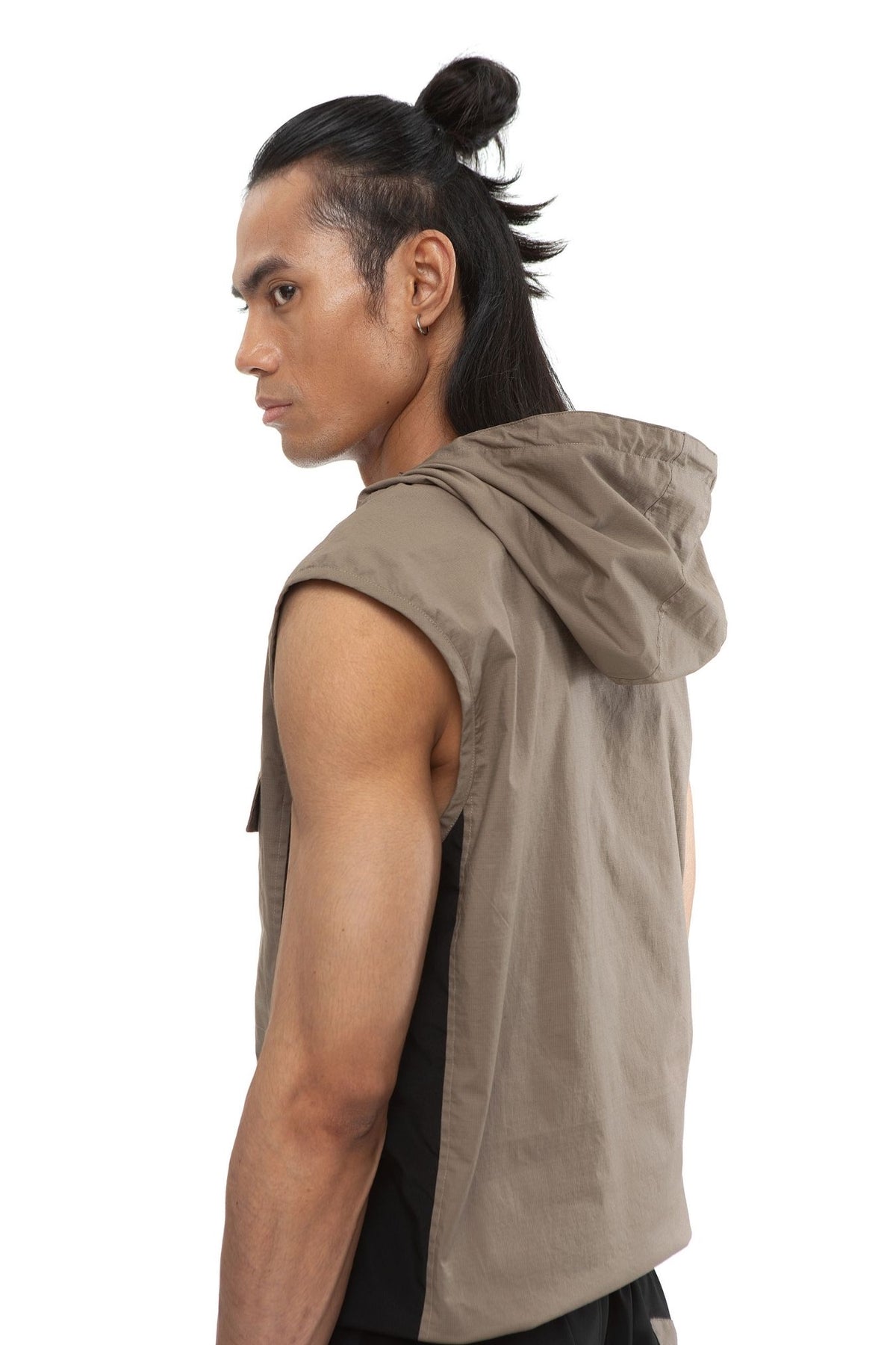 Model wearing taupe sleeveless hooded vest with quarter-zip and flap chest pockets, black contrast side paneling visible.