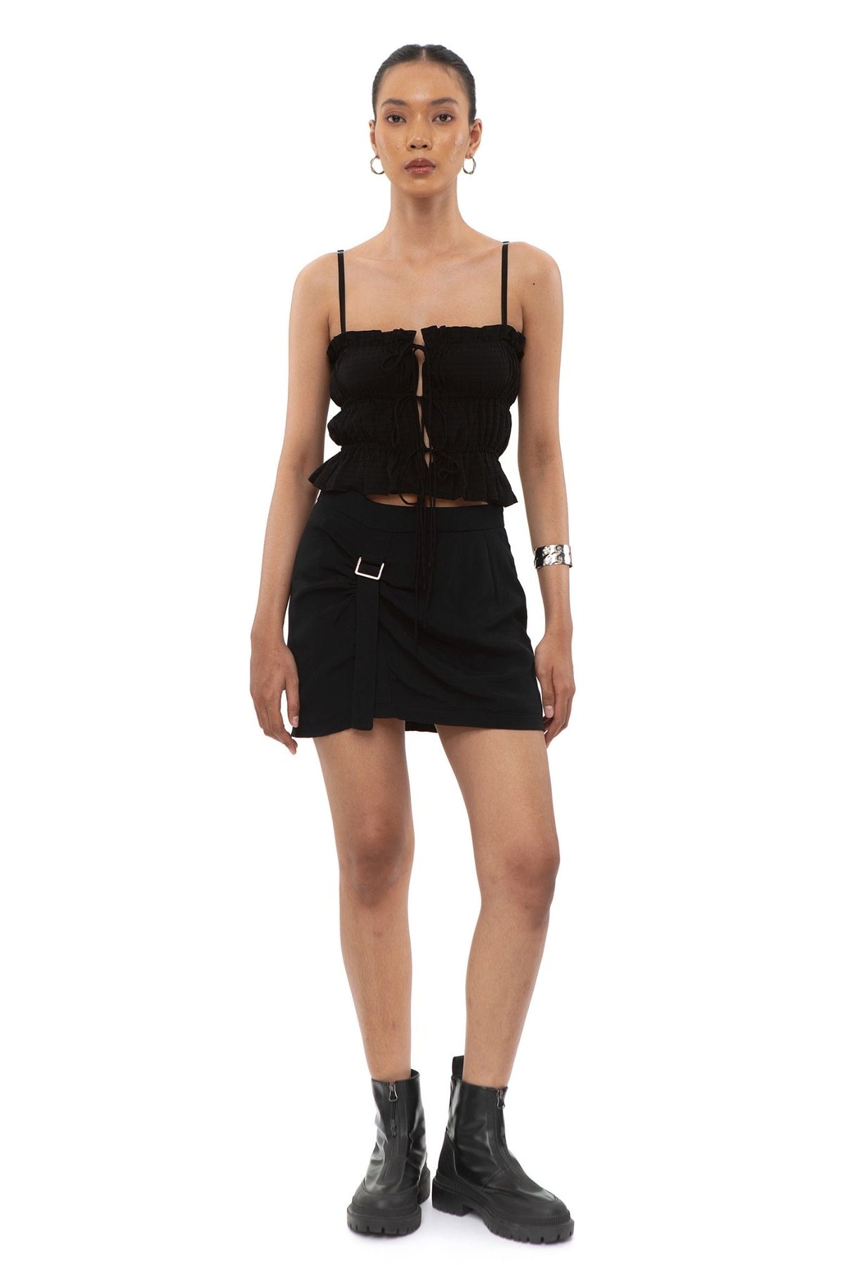 Close-up of black mini skirt with ruched front panel and metal buckle strap detail at the hip.