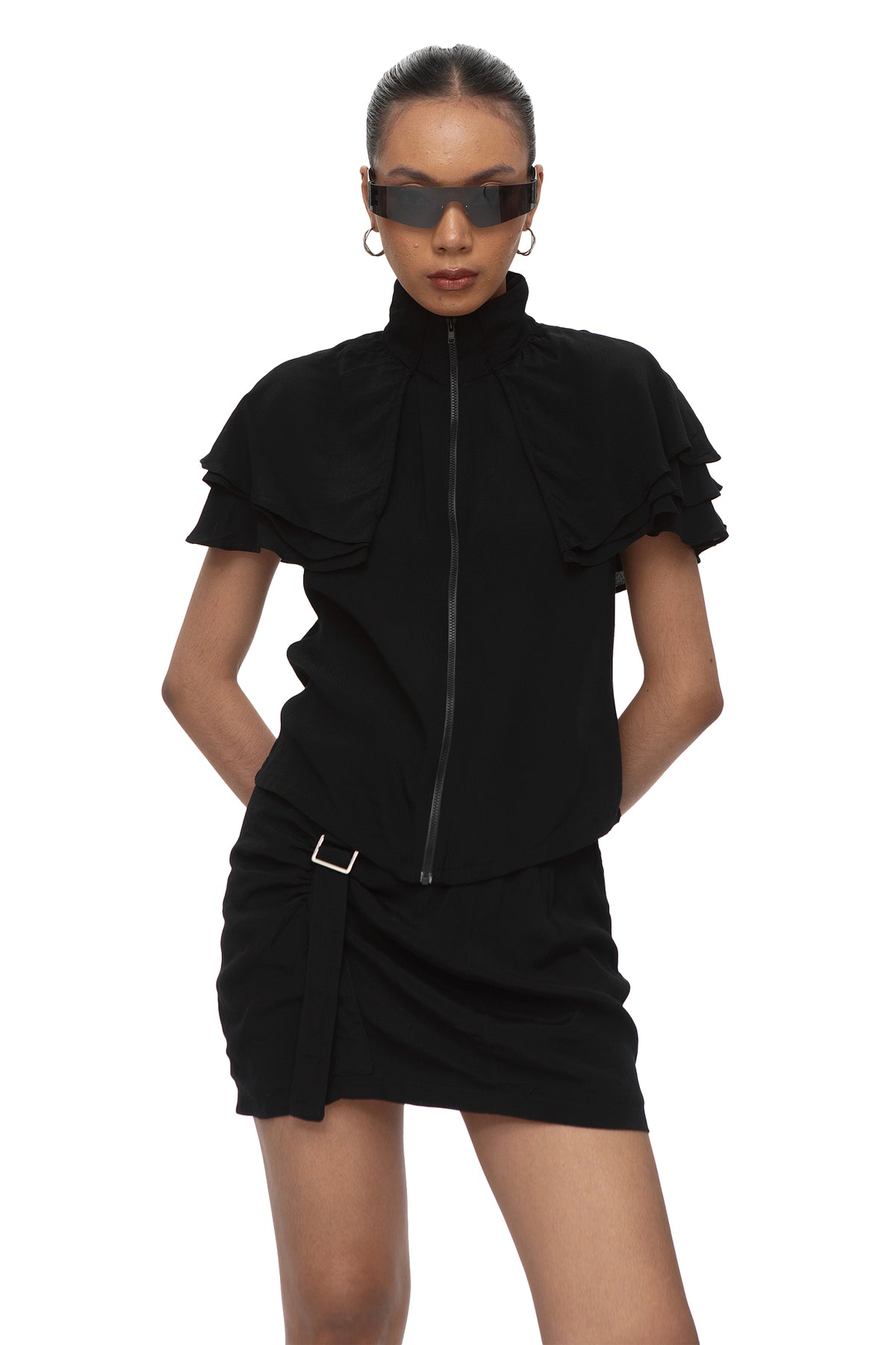Model wearing black zip top with tiered ruffle cap sleeves and high stand collar, styled with a black mini skirt